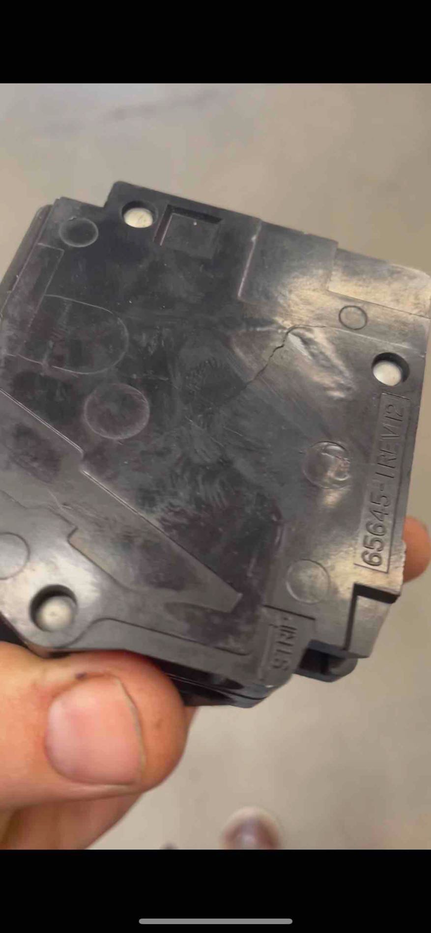 Removed electrical breaker with a visible crack in its dark casing